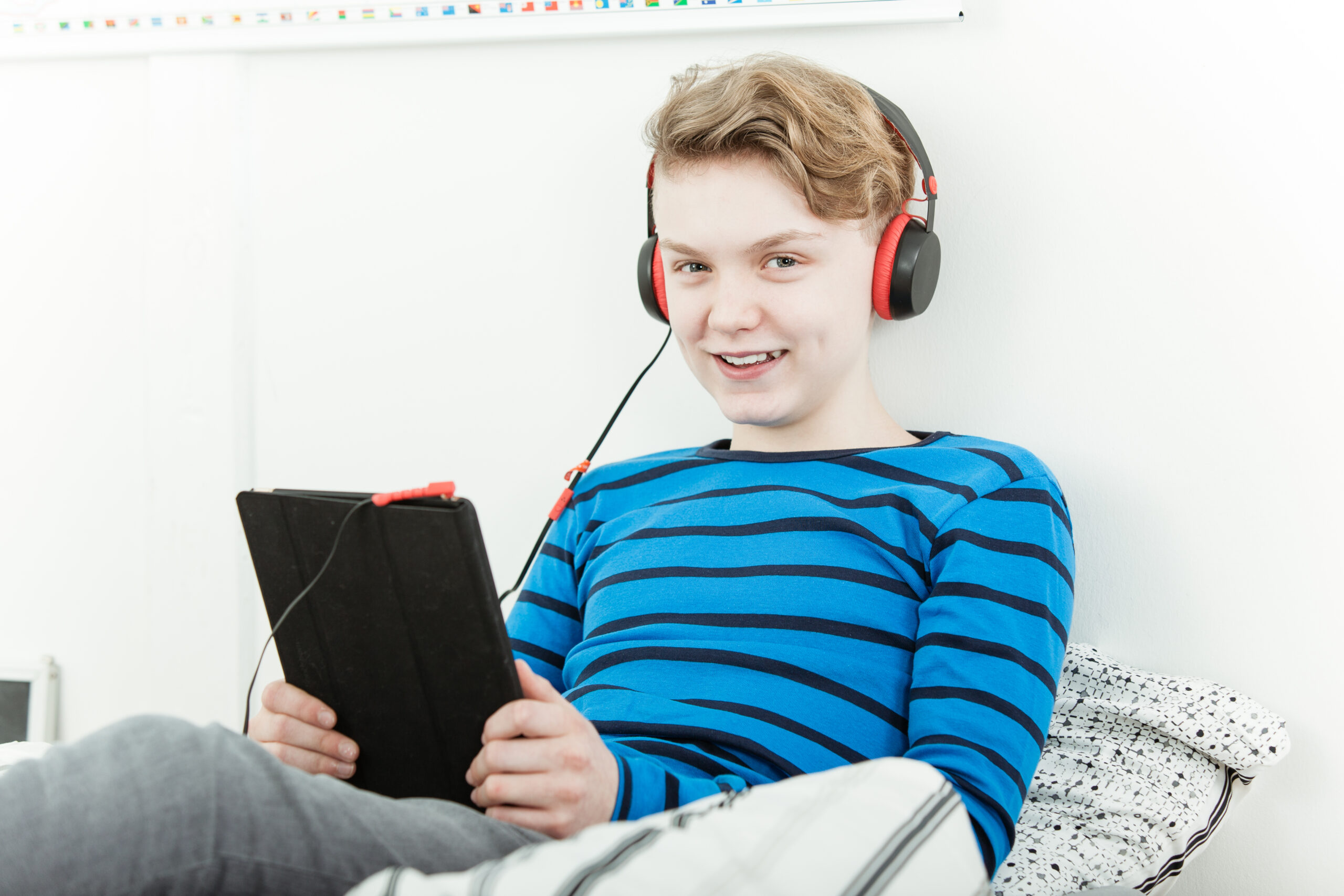 Boy with red headphones and a tablet looking at the camera and smiling.